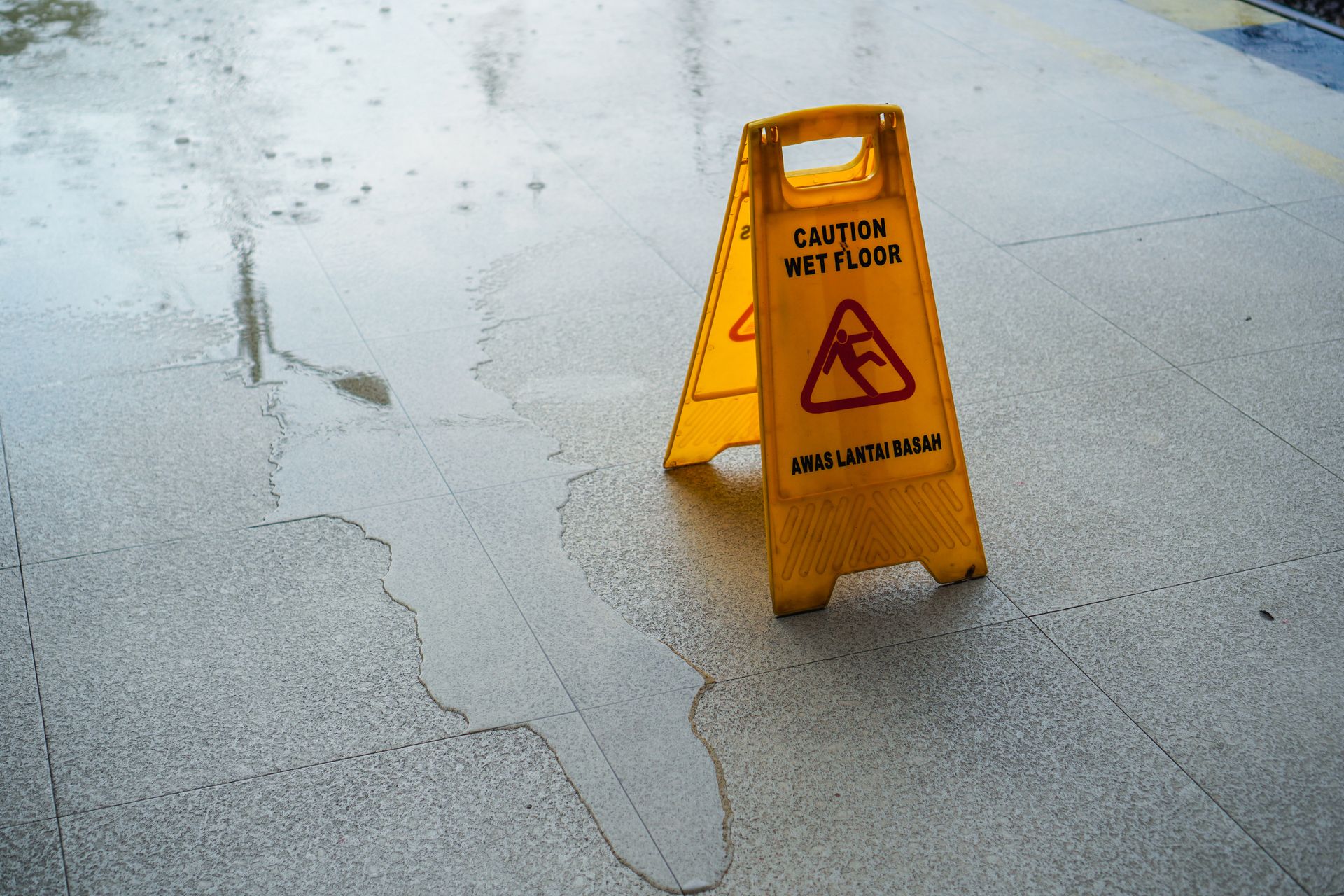 Wet floor caution sign standing on a tiled floor with visible water and spill hazards nearby.