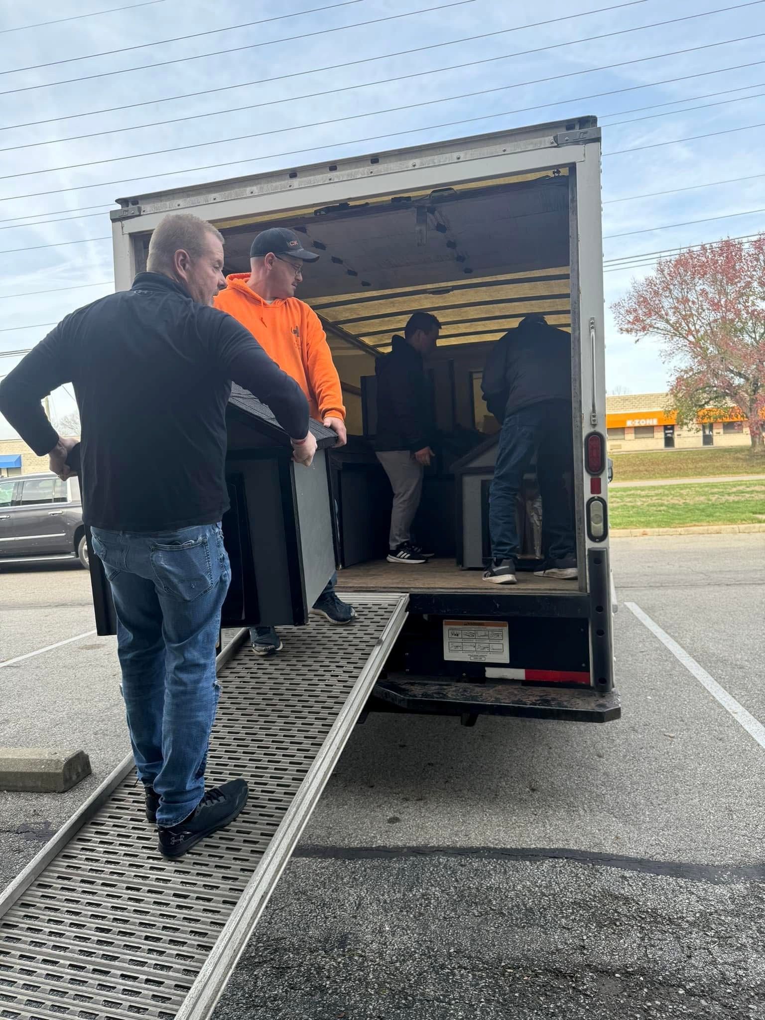 People loading items into a box truck via a ramp in a parking lot