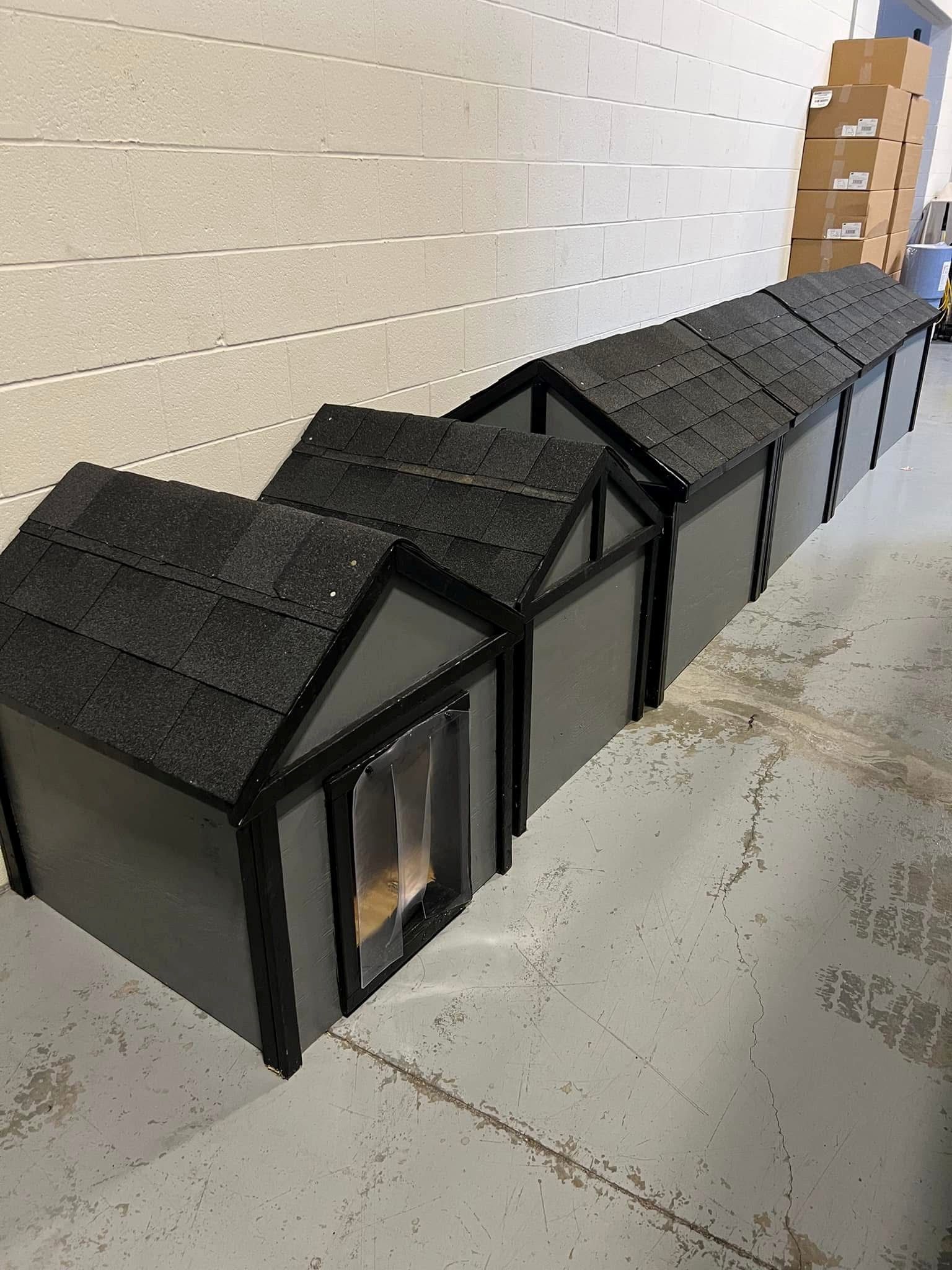 Row of black miniature house models lined up along a white wall on a concrete floor