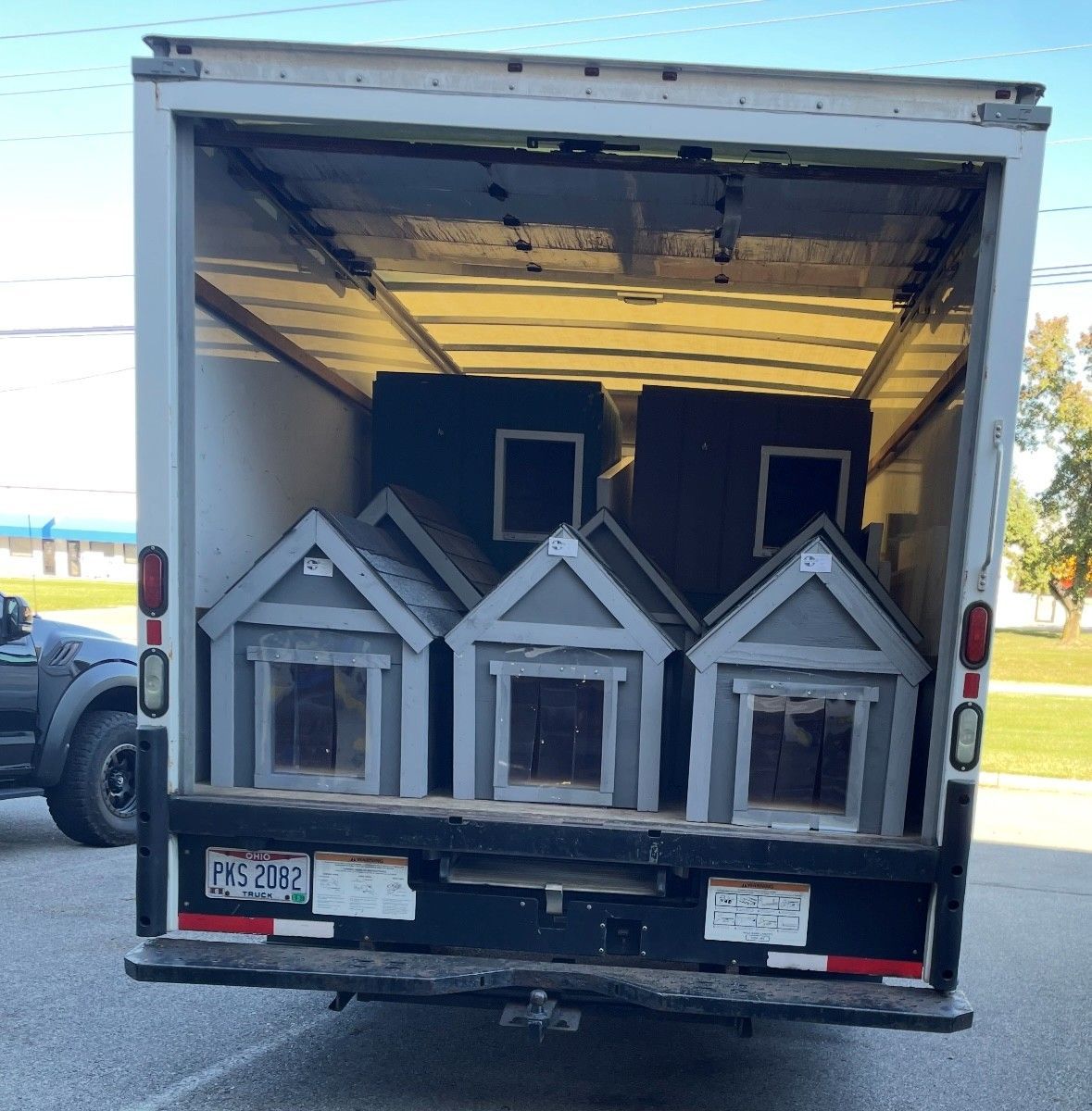 Box truck loaded with three gray doghouses and a dark structure inside the open cargo area