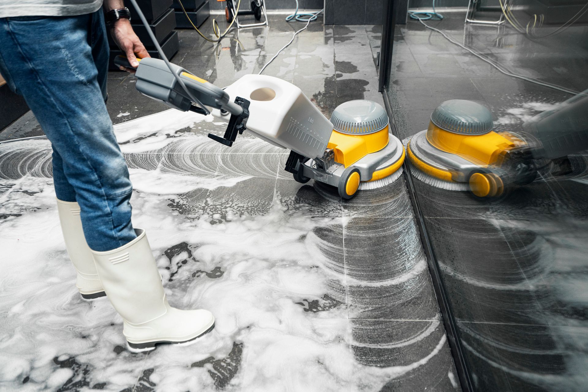 Person using cleaning machine on a wet, foamy floor. Two other cleaning robots are nearby.