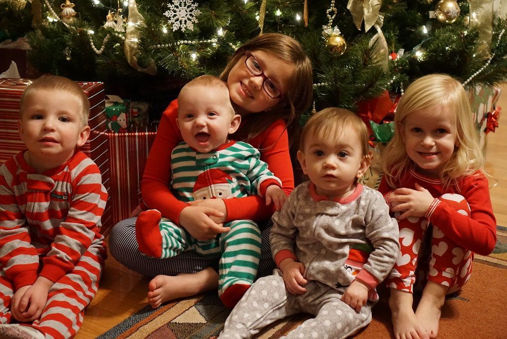 A group of children are sitting in front of a christmas tree.