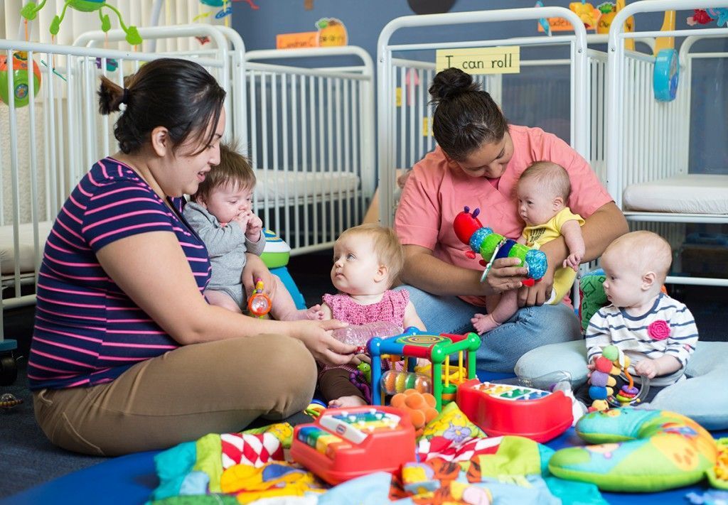 A group of women are sitting on the floor playing with babies.