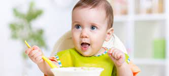 A baby is sitting in a high chair eating food with a spoon.
