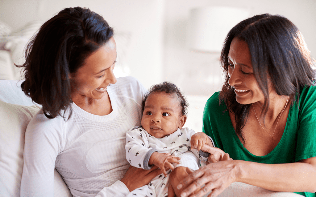 Two women are sitting on a couch holding a baby.