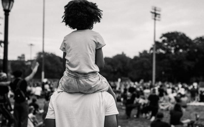 A black and white photo of a man carrying a child on his shoulders.