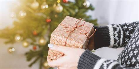A woman is holding a christmas present in front of a christmas tree.