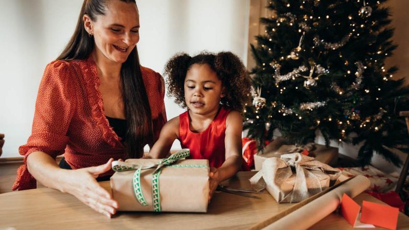 A woman and a little girl are wrapping christmas presents in front of a christmas tree.