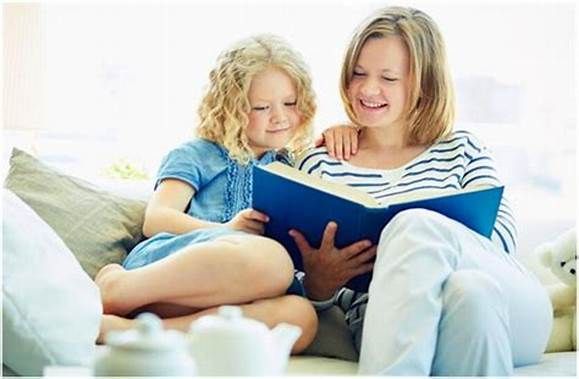 A woman and a little girl are sitting on a couch reading a book.