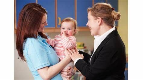 Two women are holding a baby and talking to each other.