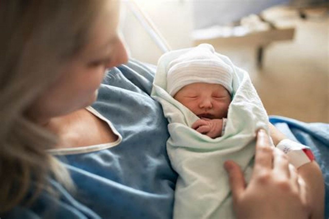 A woman is holding a newborn baby wrapped in a blanket.