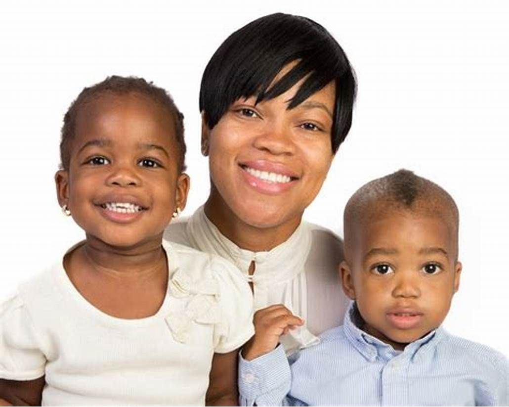 A woman is holding two children and smiling for the camera.