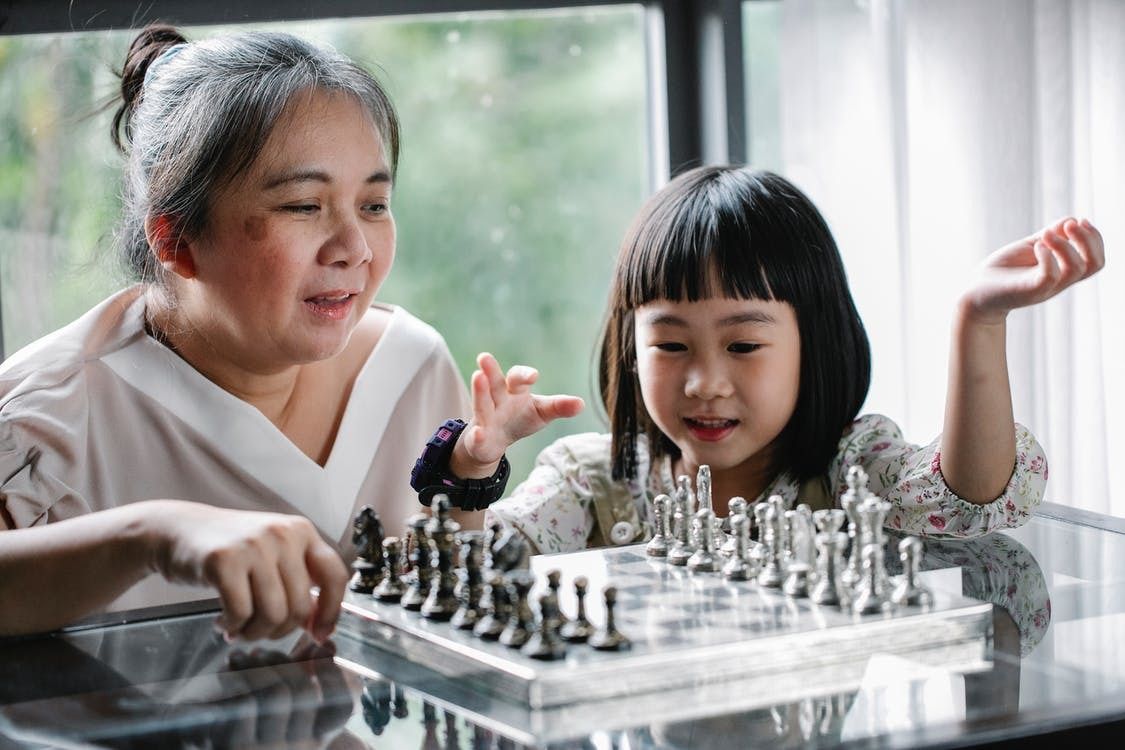 An elderly woman and a young girl are playing a game of chess.