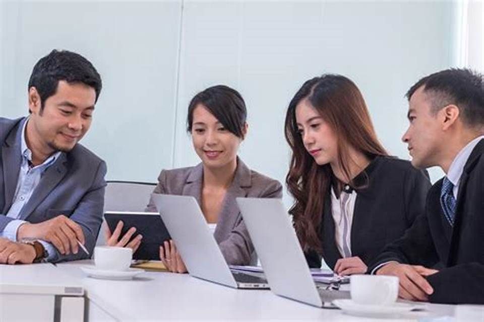 A group of business people are sitting around a table looking at laptops and a tablet.