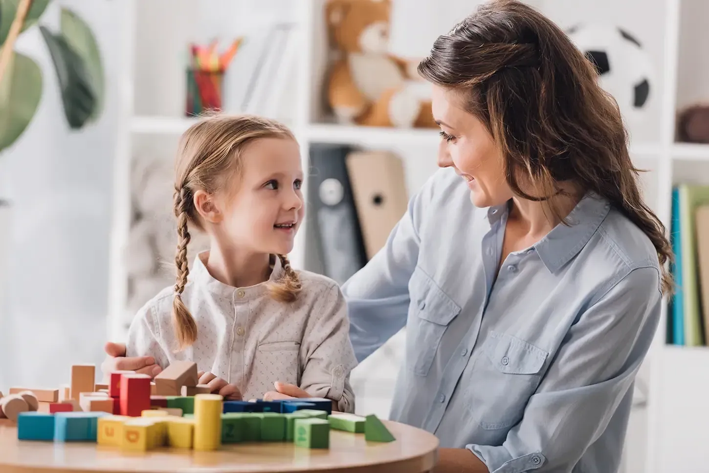 A woman and a little girl are playing with wooden blocks at a table.