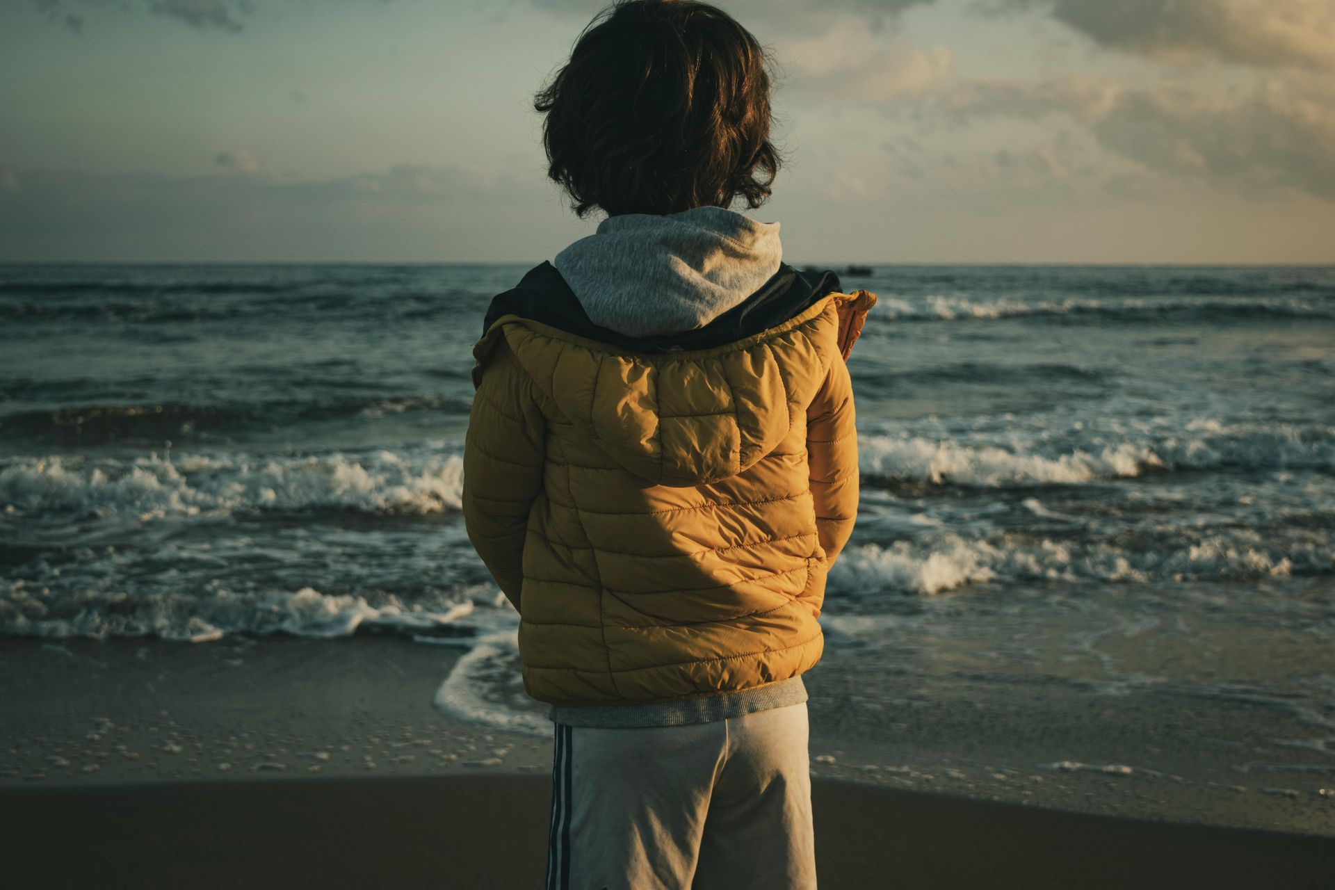 A young boy is standing on a beach looking at the ocean.
