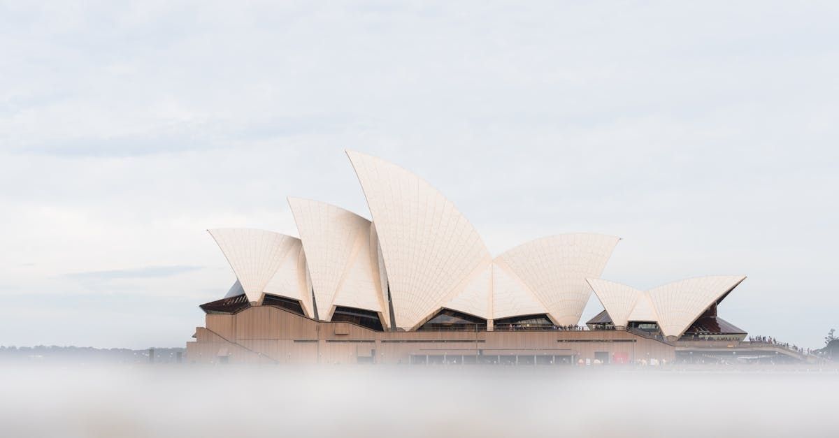 The sydney opera house is surrounded by fog on a cloudy day.
