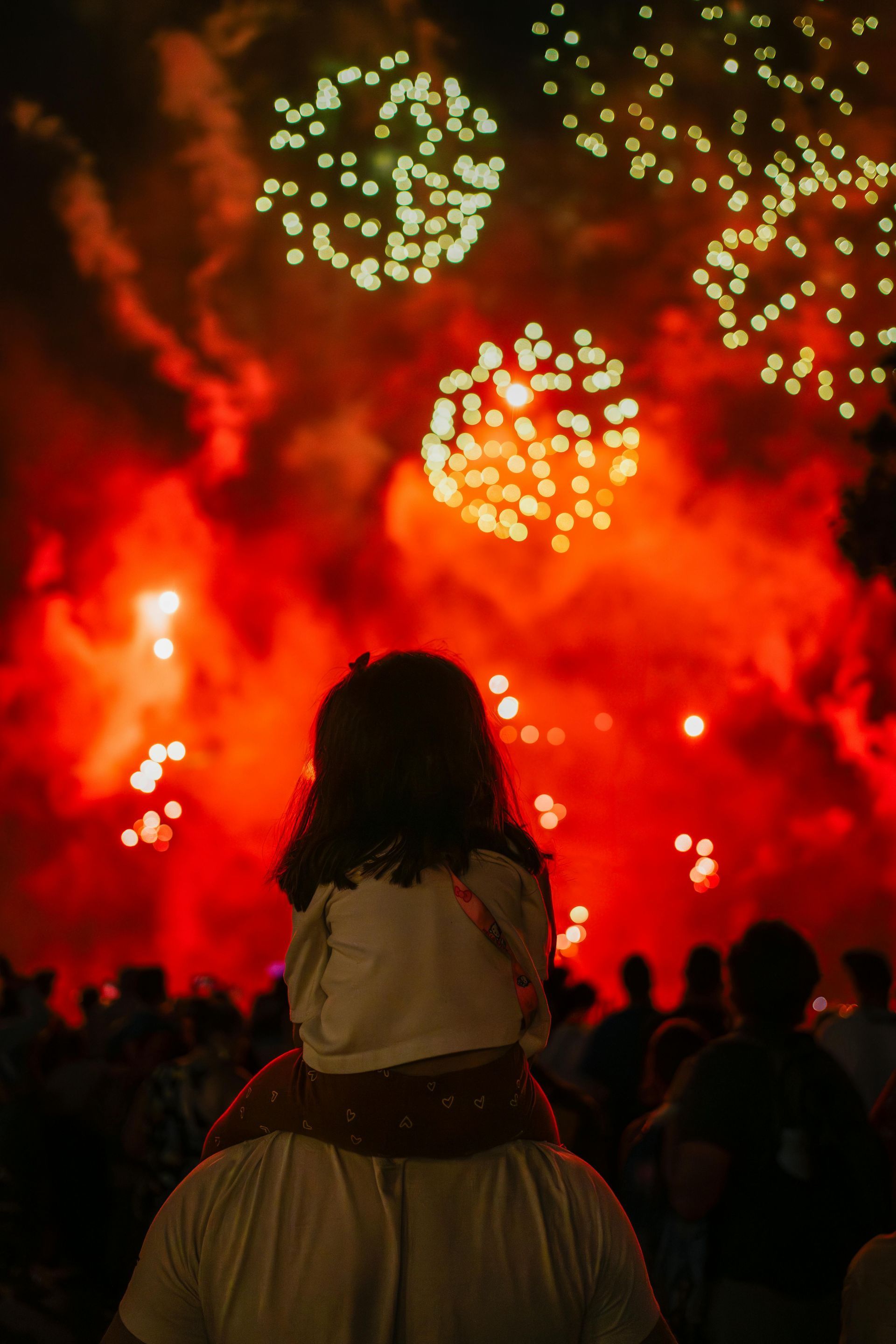 A little girl is sitting on a man 's shoulders watching fireworks.