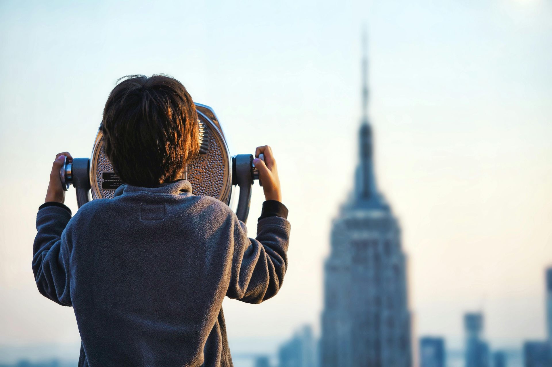 A person is looking through binoculars at the empire state building.