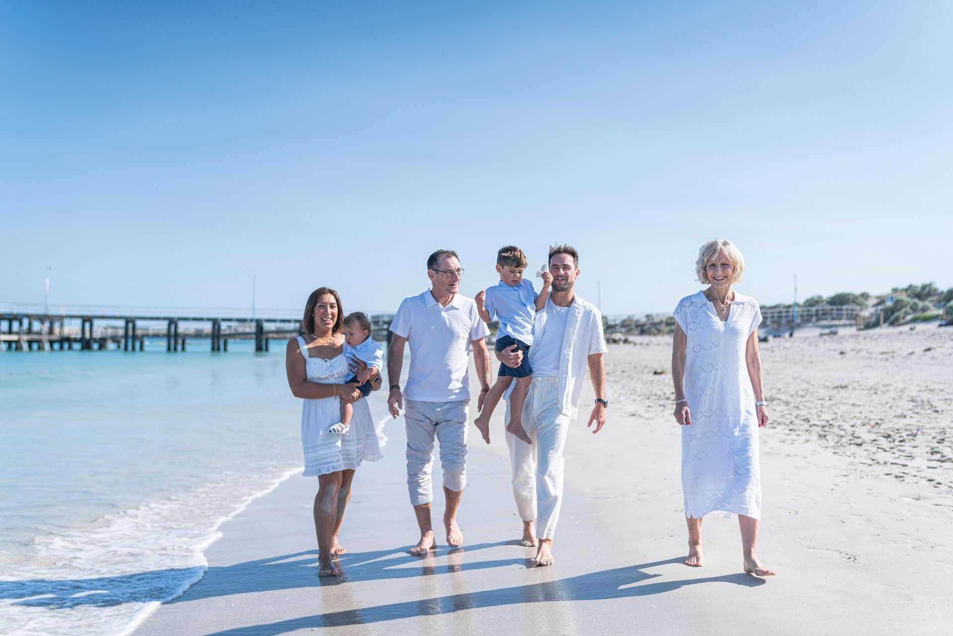 A family in white clothes is walking on the beach.
