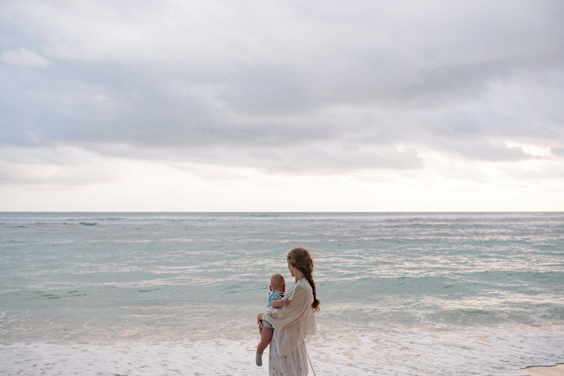 A woman is holding a baby on the beach.