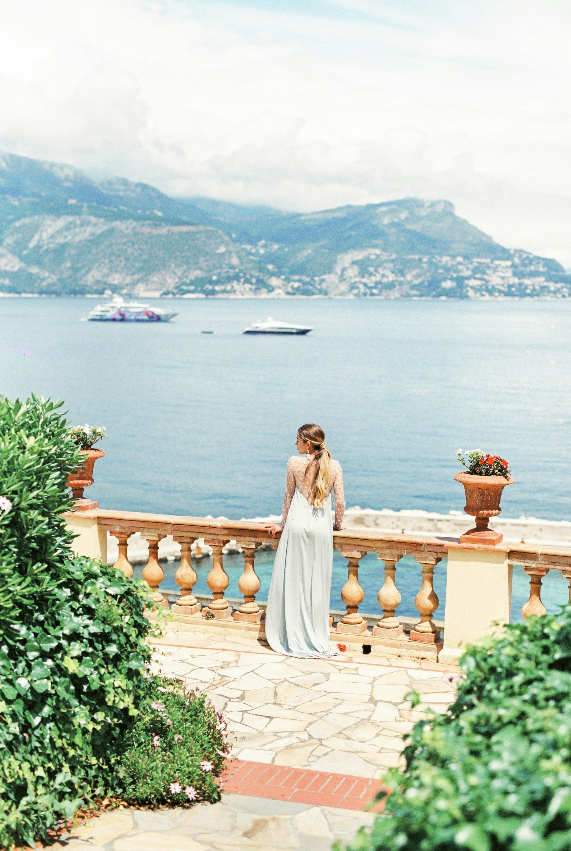 A bride and groom are standing on a balcony overlooking the ocean.