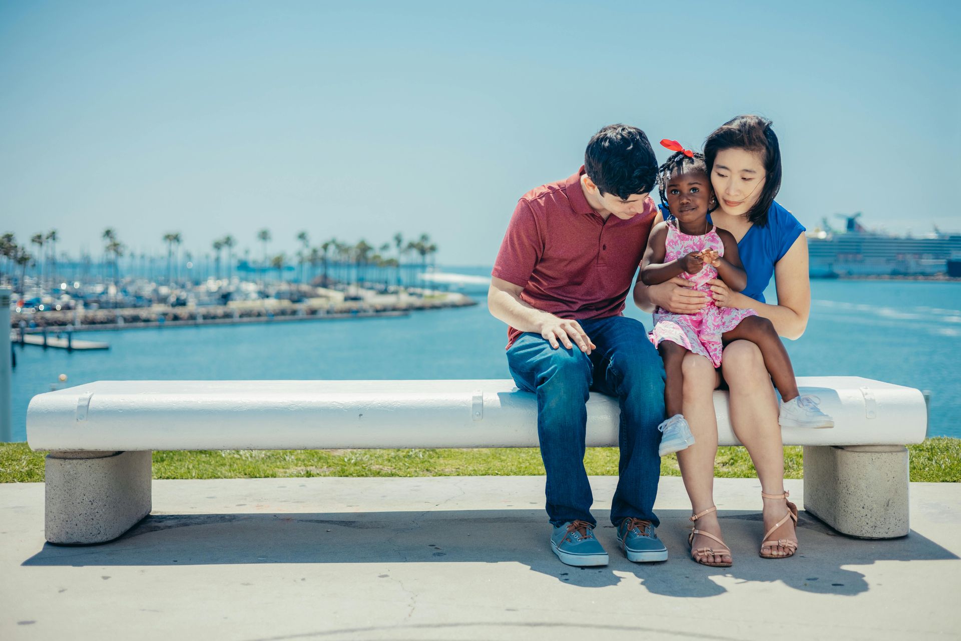 A man and woman are sitting on a bench with a little girl.