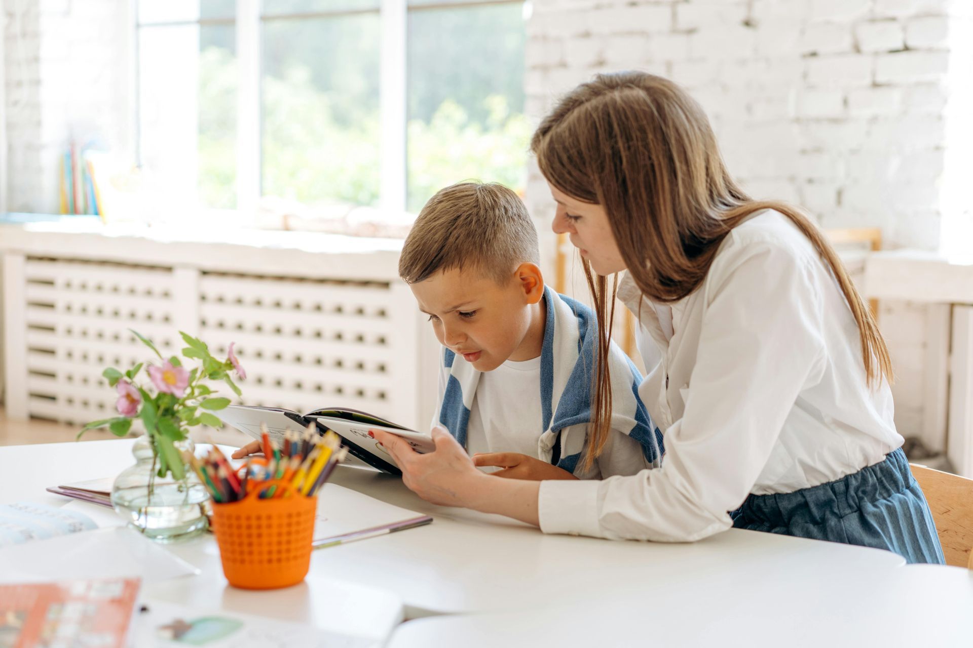 A woman and a boy are sitting at a table looking at a tablet.