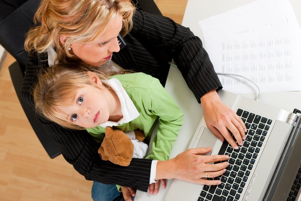 A woman is holding a little girl while using a laptop computer.
