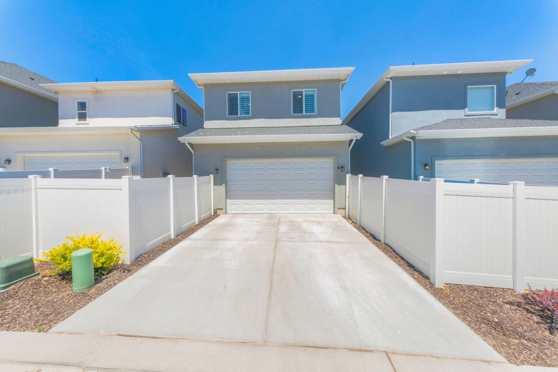 A driveway leading to a house with a white fence