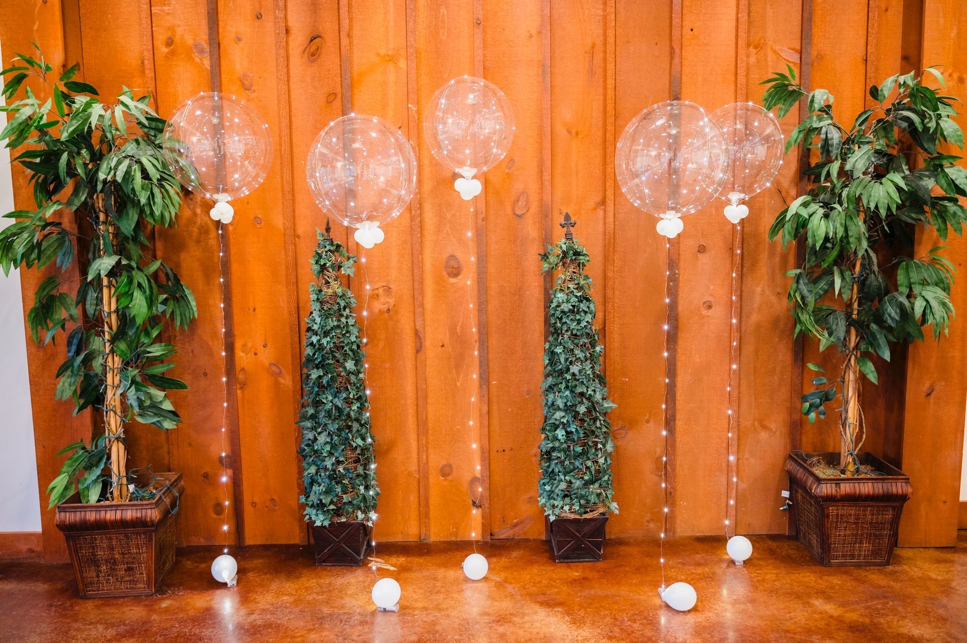 Decorative wooden backdrop with hanging lights, small lit trees, and potted plants on a polished floor