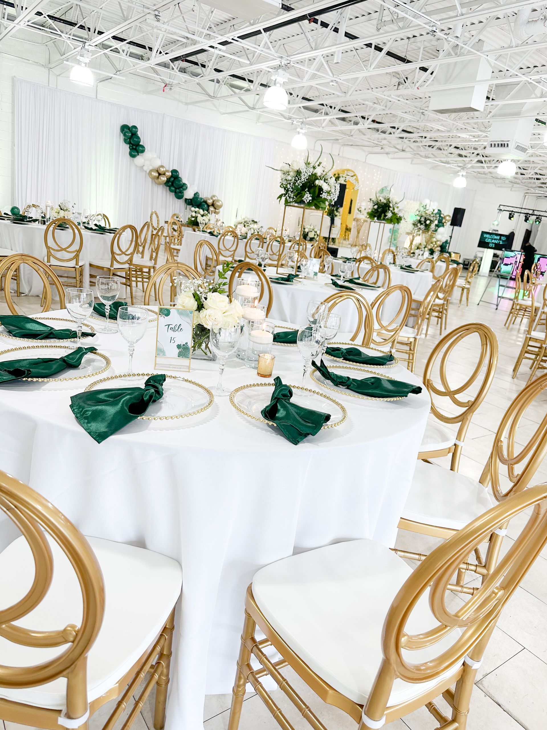 Elegant banquet hall with round white tables, gold chairs, and green napkins set for an event