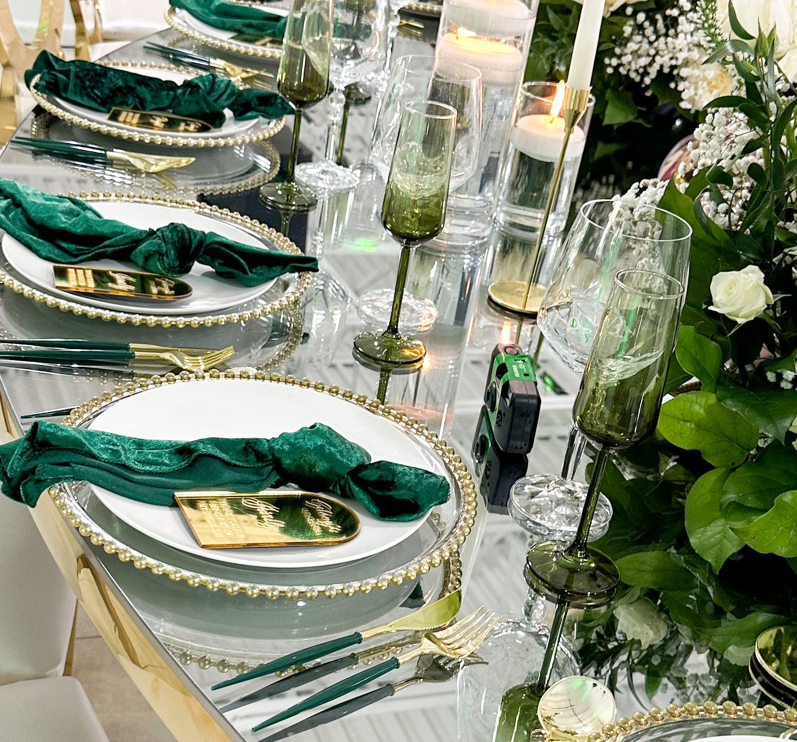 Elegant banquet table with white plates, green napkins, gold accents, candles, and floral decor