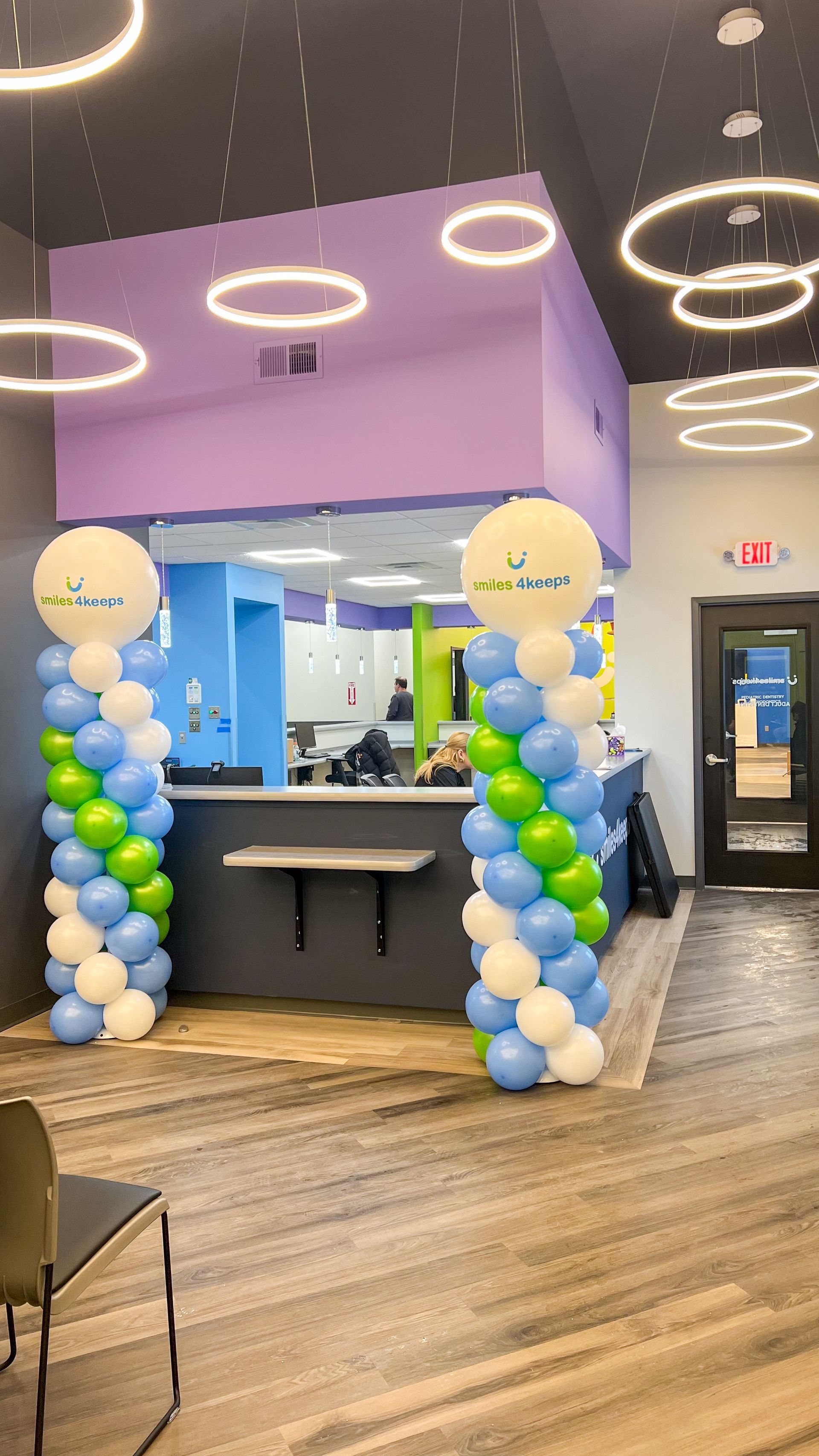 Decorated reception desk with blue and white balloon columns and hanging ring lights in a modern lobby