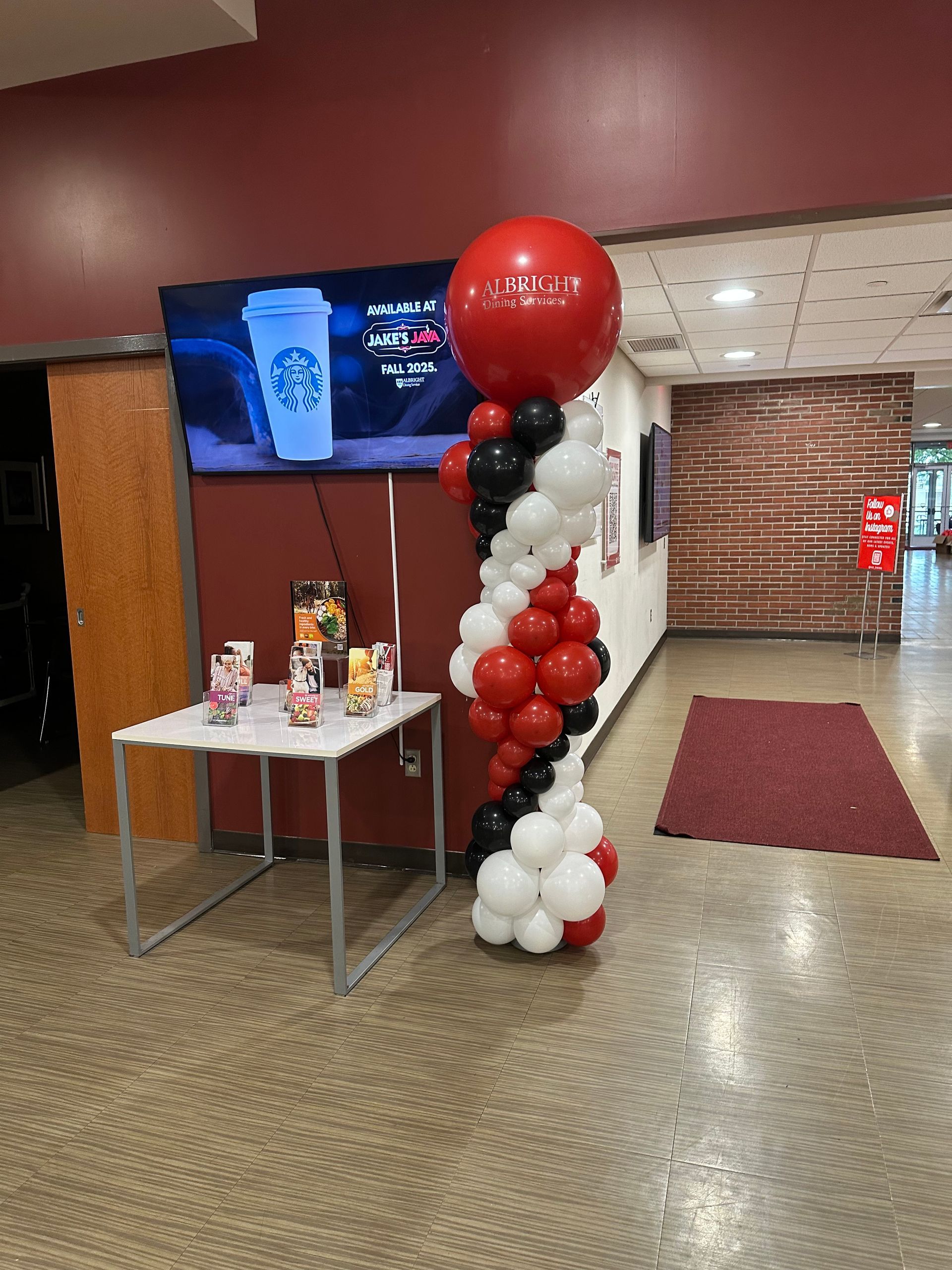 Balloon display beside a small table in a hallway with a TV screen and red carpet runner.