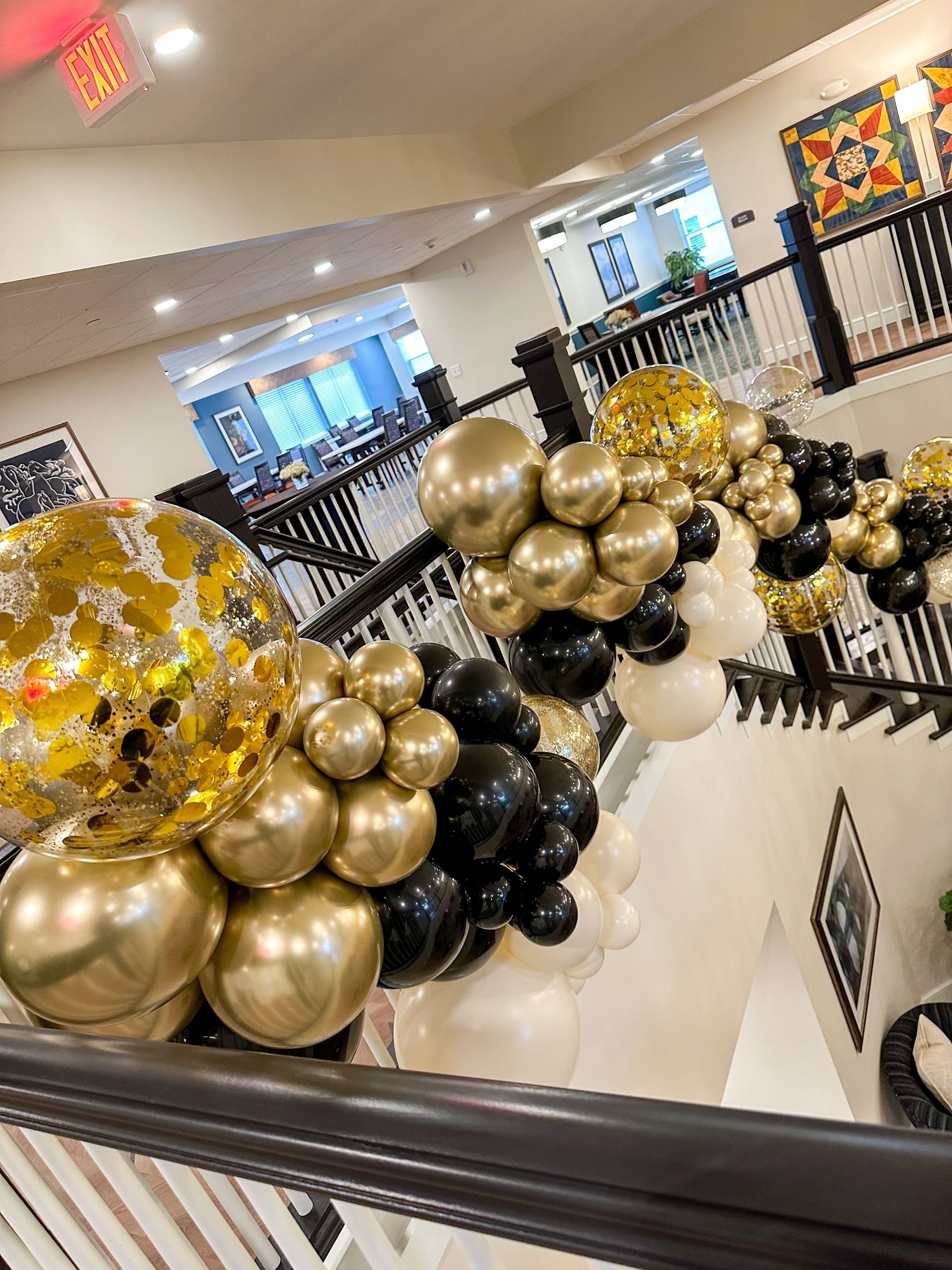 Black, gold, and clear balloon decorations along a stair railing in a bright indoor lobby