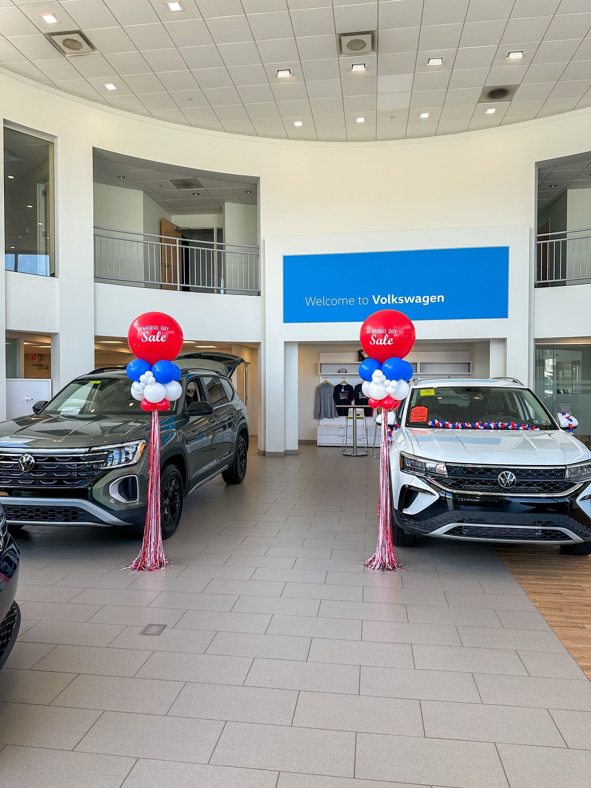 Two cars in a car dealership, with red, white, and blue balloon columns in front of them.