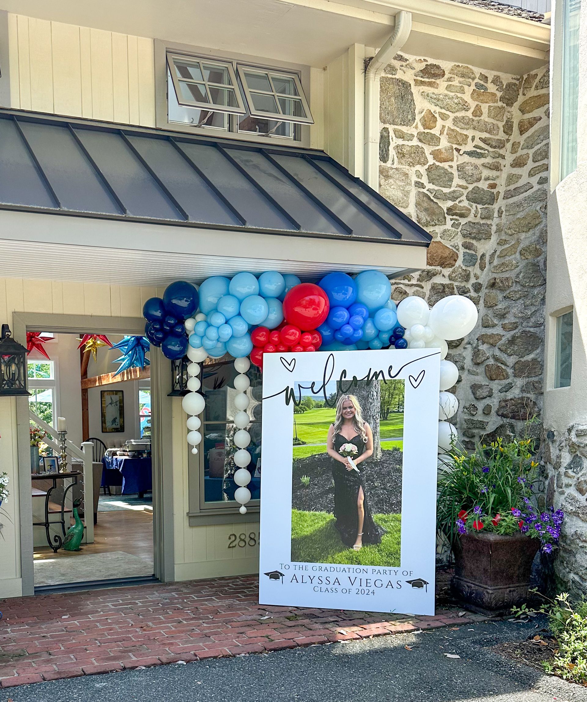 Entrance decorated with balloons and a photo of a person; outside a building with stone and brick details.