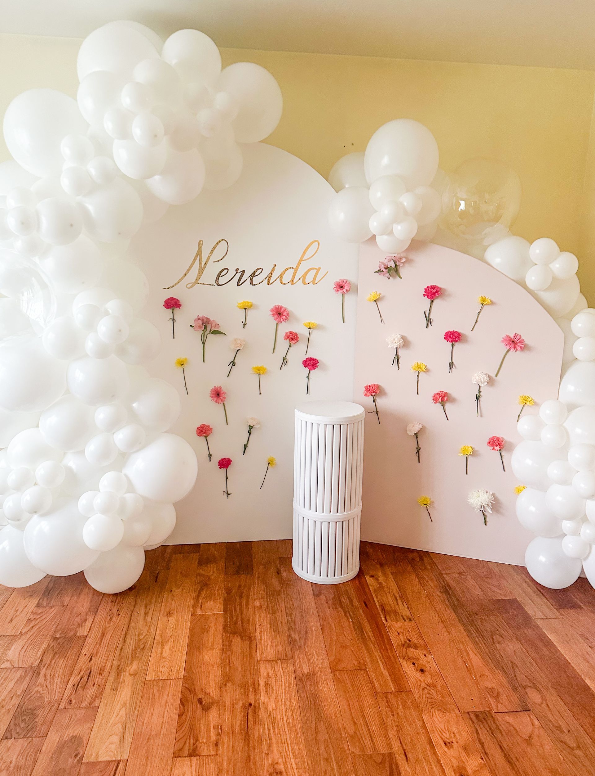 Pink and white backdrop with balloons, flowers, and a gold name