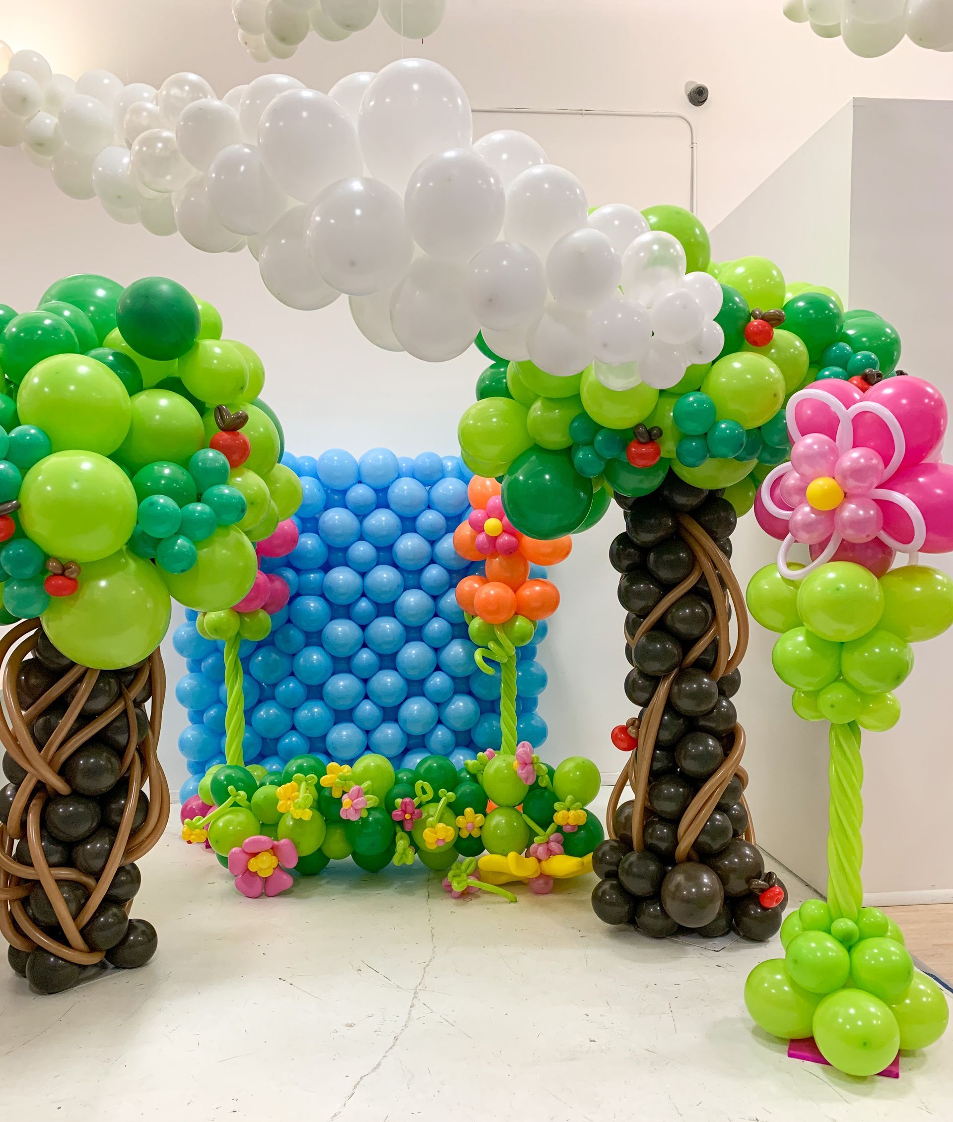 Balloon art display featuring trees, flowers, and a blue wall backdrop, all made of colorful balloons.