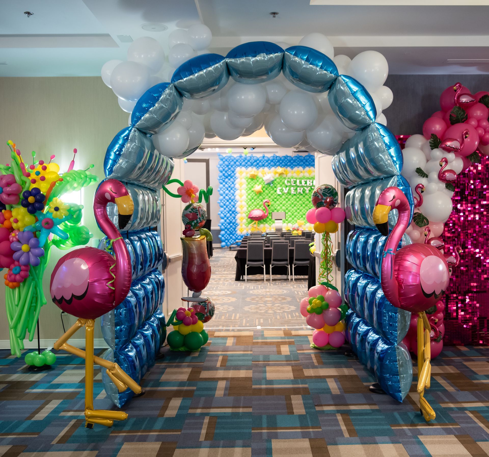 Festive doorway arch with blue and white balloons, flamingo decorations, leading to an event room.