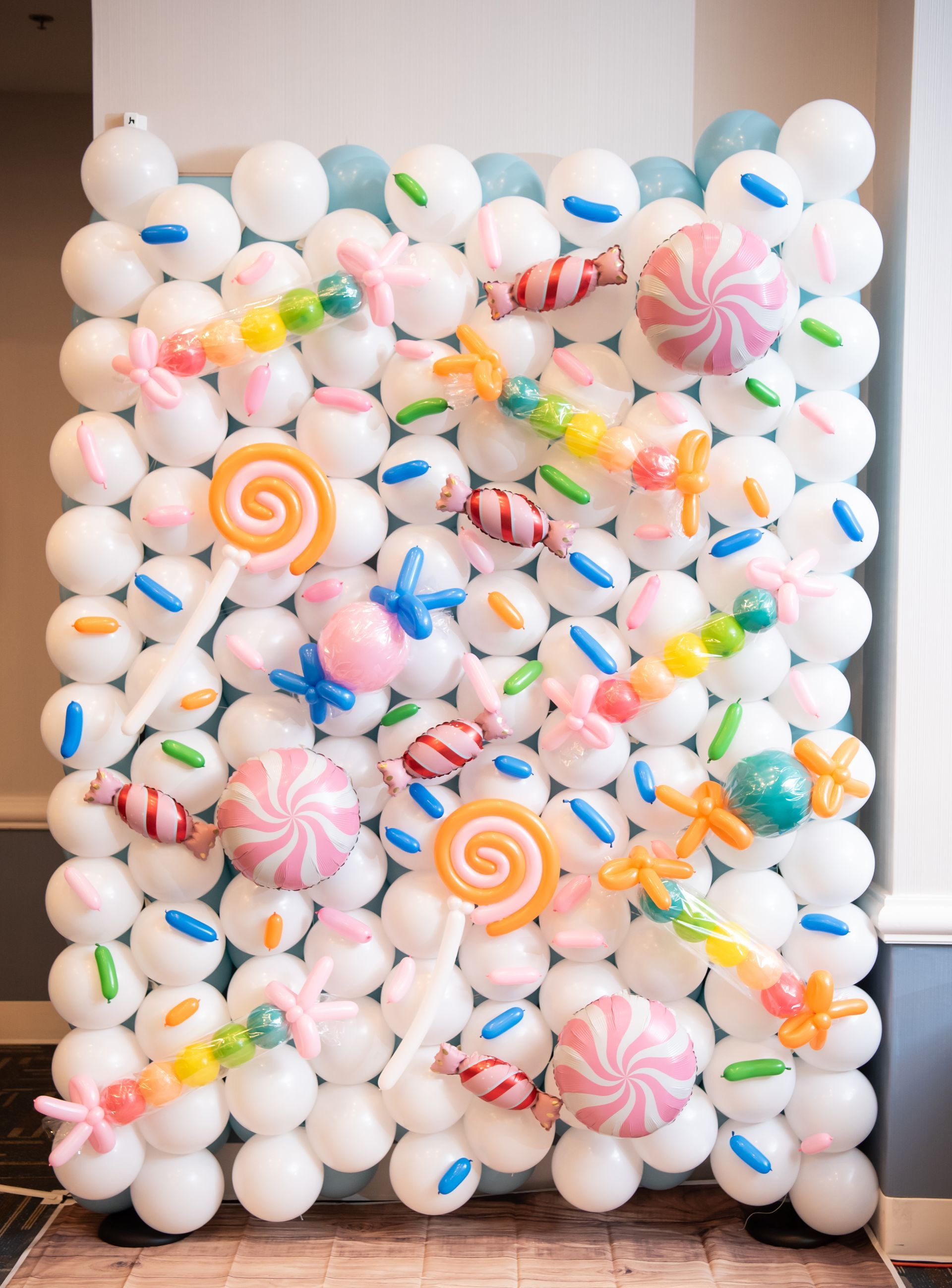Candy-themed balloon wall with white and blue balloons, and candy-shaped balloons in various colors.