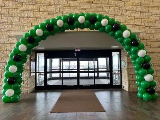 Green, black, and white balloon arch over glass doors.