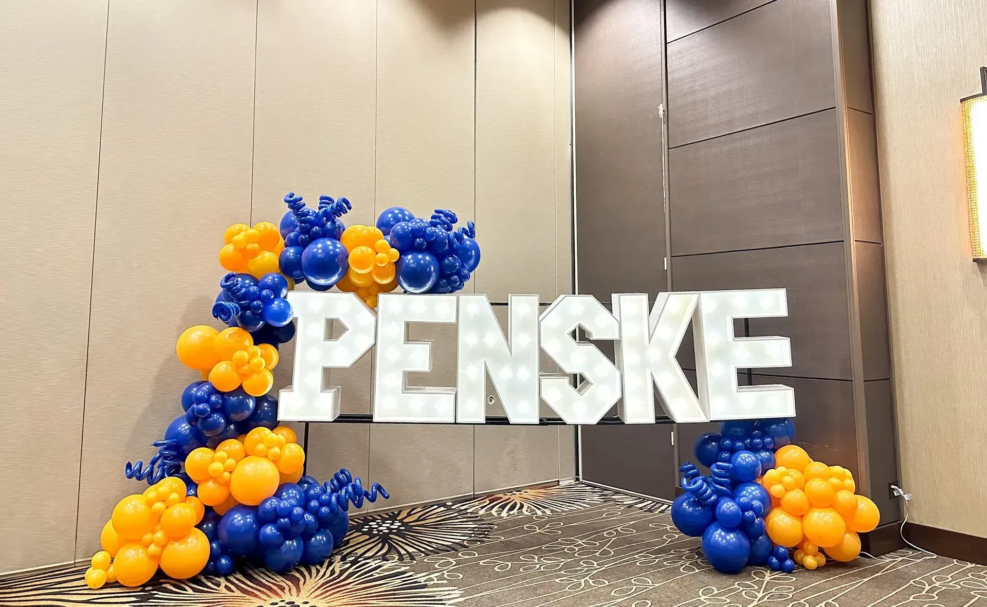 Penske sign surrounded by blue and orange balloon decorations at an indoor event