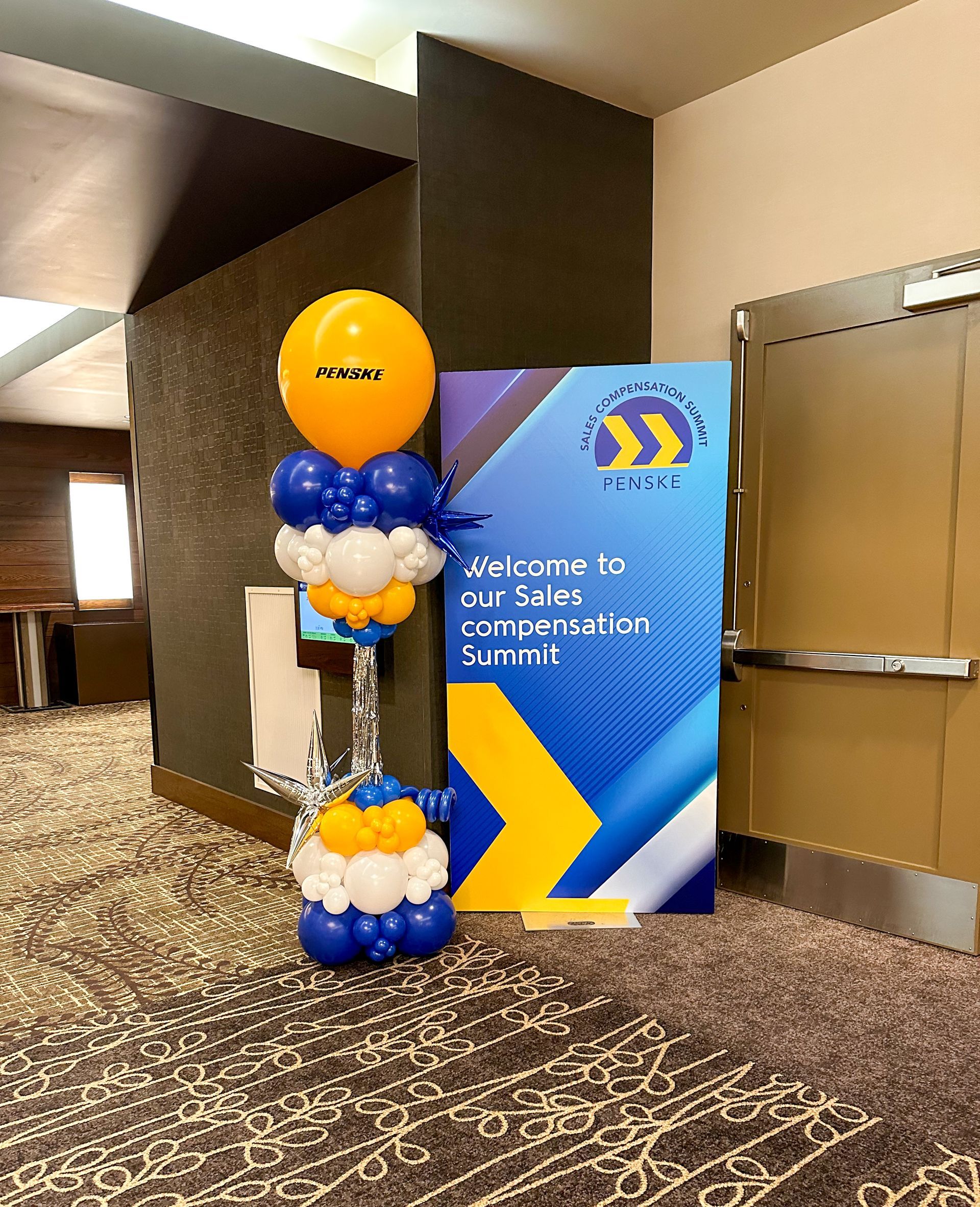 Balloon display beside a blue welcome sign in a hotel hallway at a conference entrance