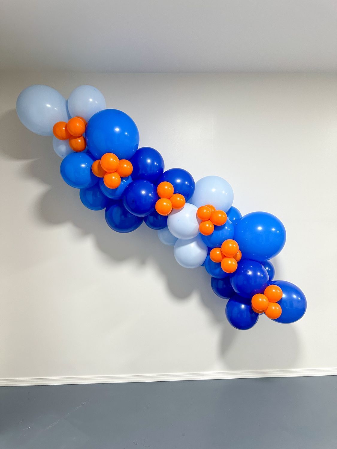 Balloon garland in shades of blue and orange, affixed to a white wall.