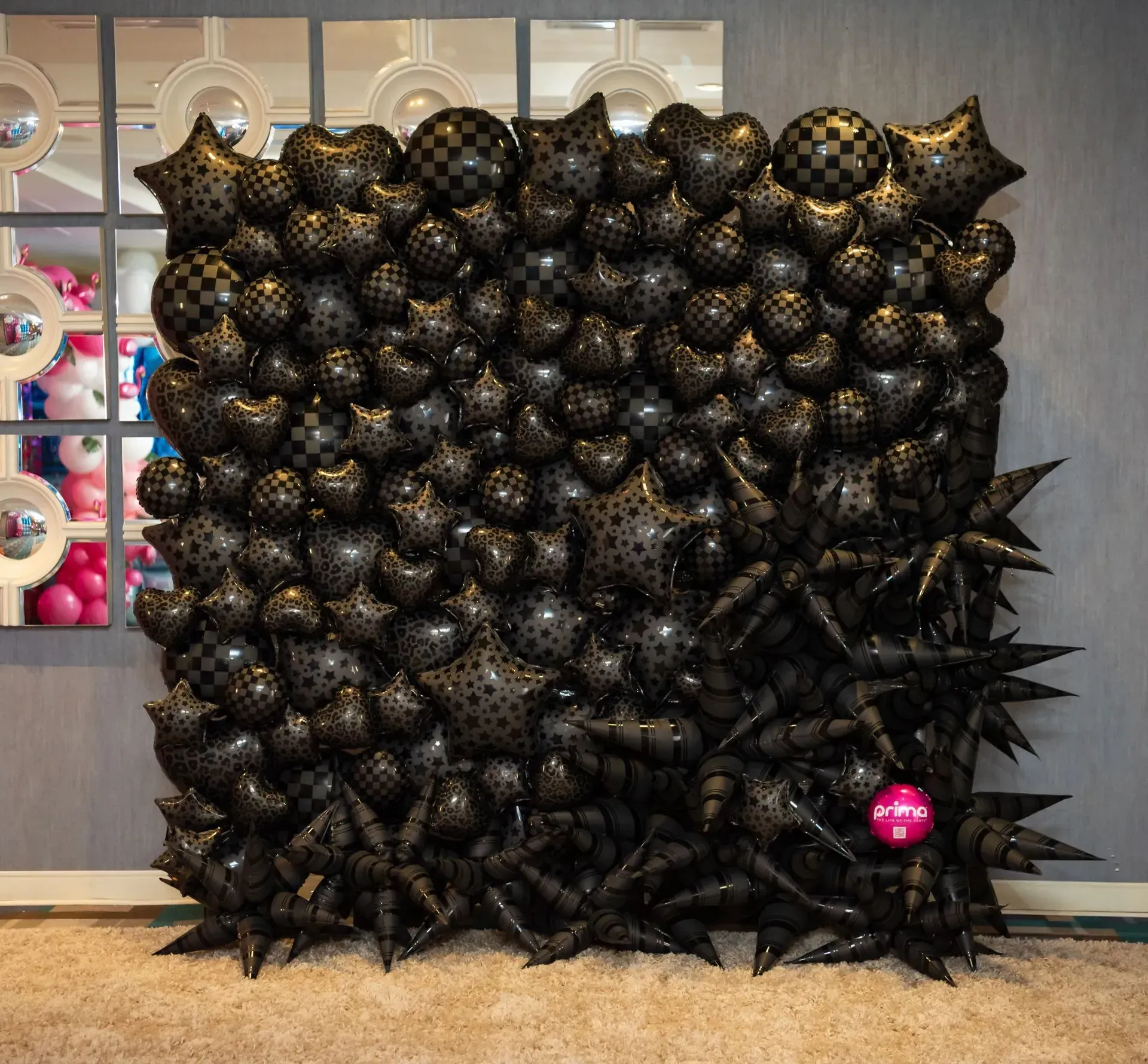 Black spiky balloon sculpture installation with a single pink balloon accent in a gallery-like space
