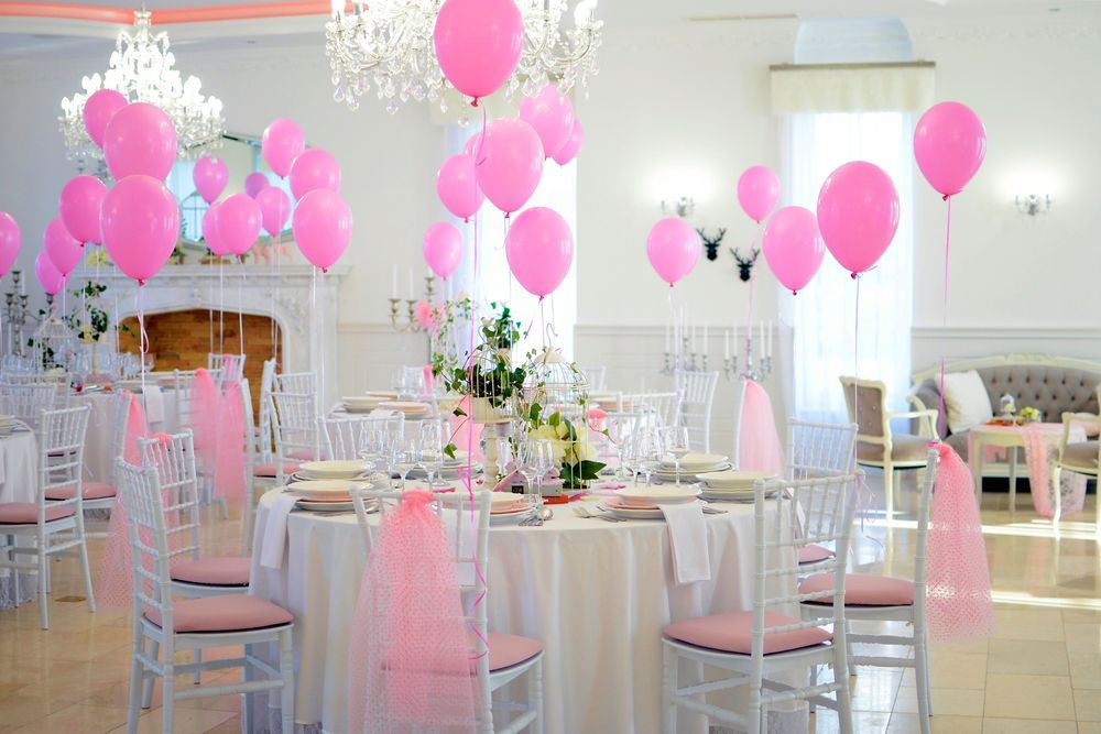 Pink balloon-decorated banquet hall with set tables and chairs for a celebration