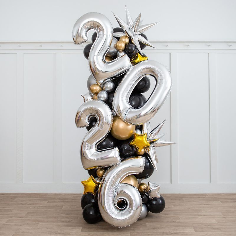 Birthday party backdrop with balloons in lavender, yellow, pink, and gold, featuring a cake and podiums.