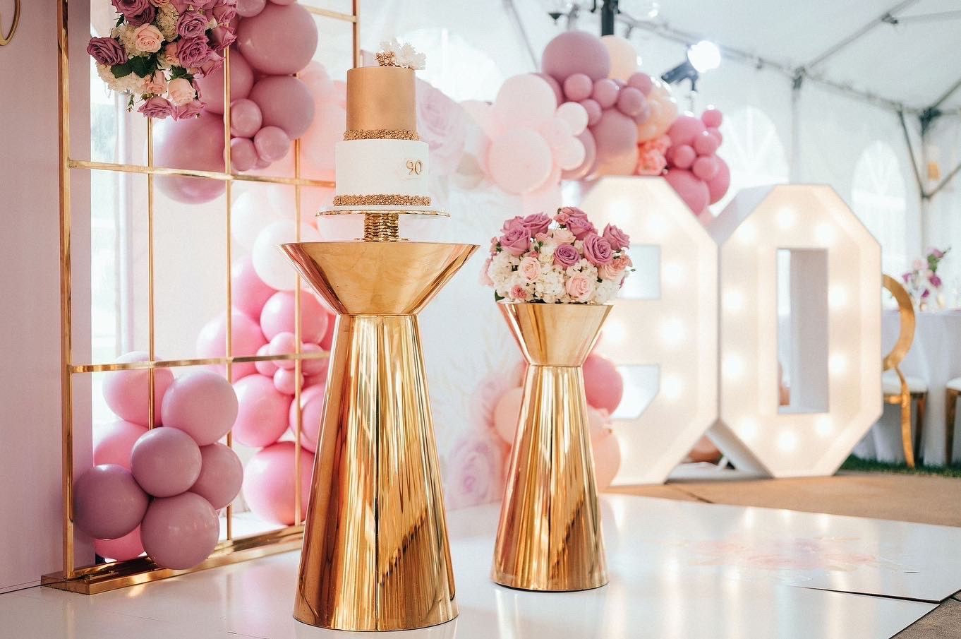 Pink and gold party decor with balloons, flowers, and illuminated letters in a bright event room